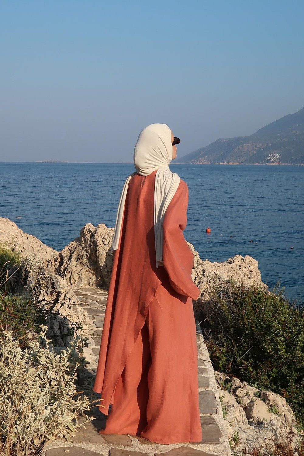 Cherianne.com terracotta oversized asymmetric linen blouse worn by a woman with a hijab by the sea